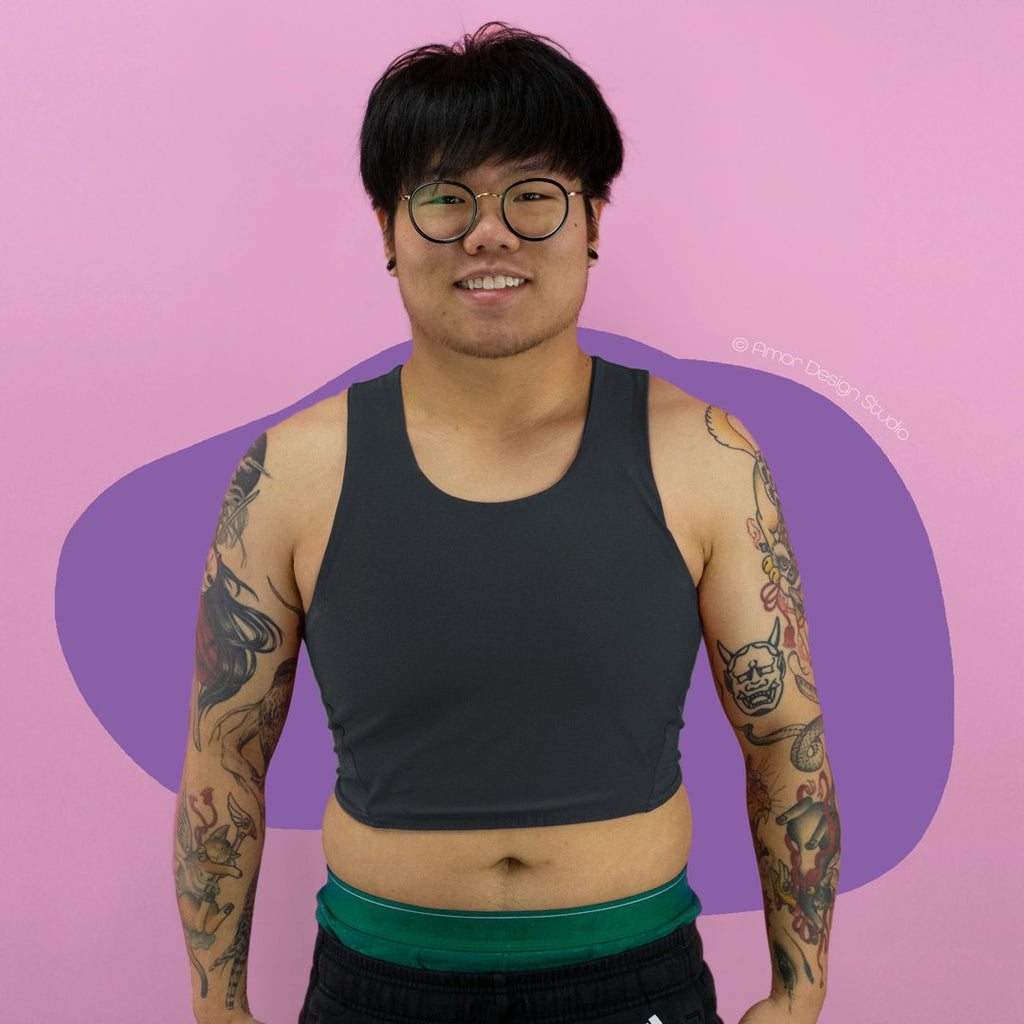 Non-binary trans person wearing a dark grey, mid length, racerback chest binder - front