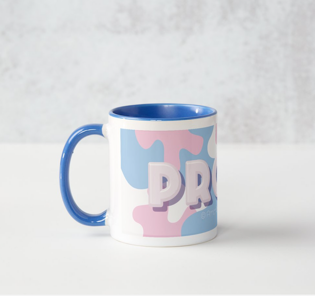 Product image of regular size mug with blue handle and interior, PROUD text in large white font over full wrap camouflage print in transgender pride colours.