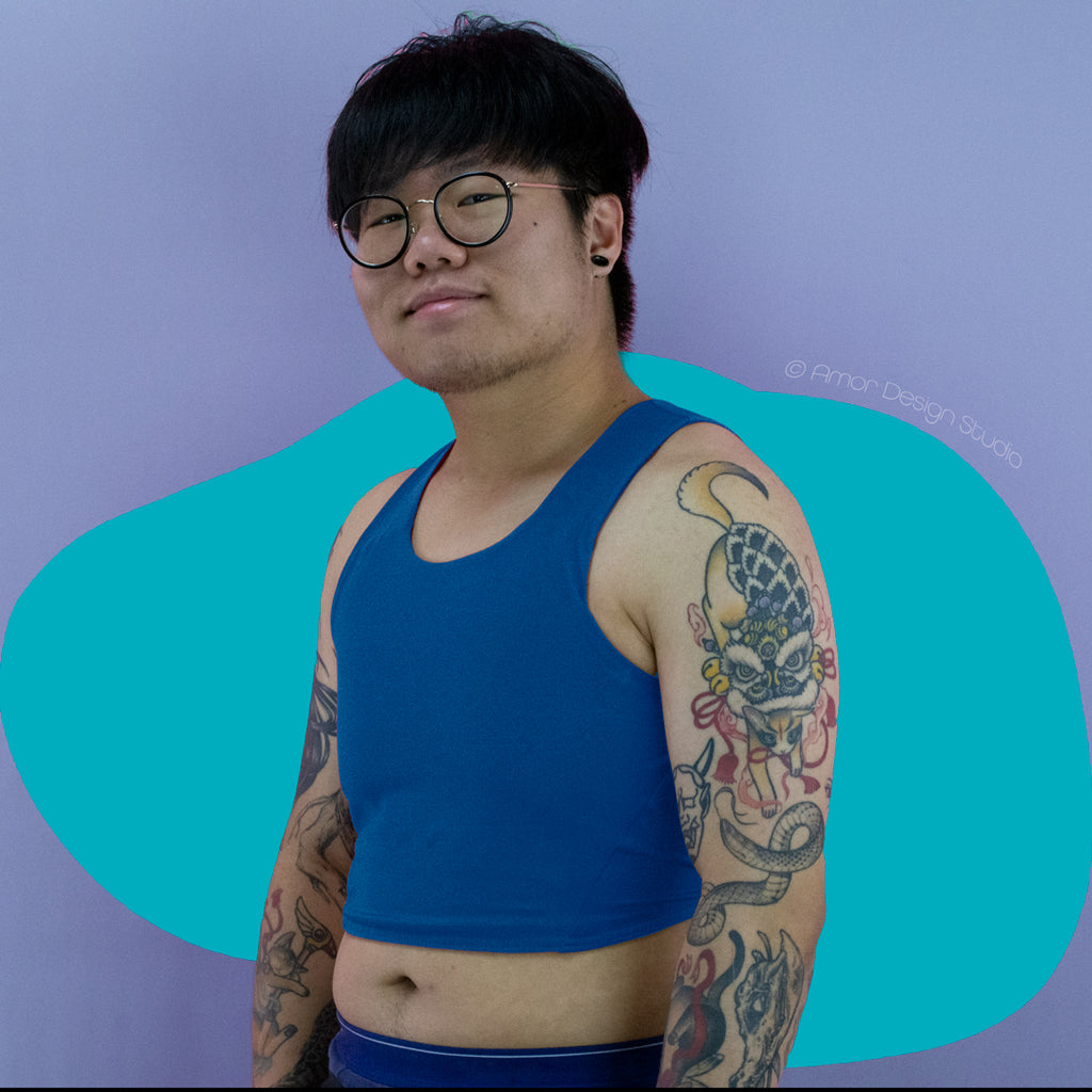 Asian non-binary trans masc person wearing reversible chest binder worn on the blue side. Colour is a mid blue. 