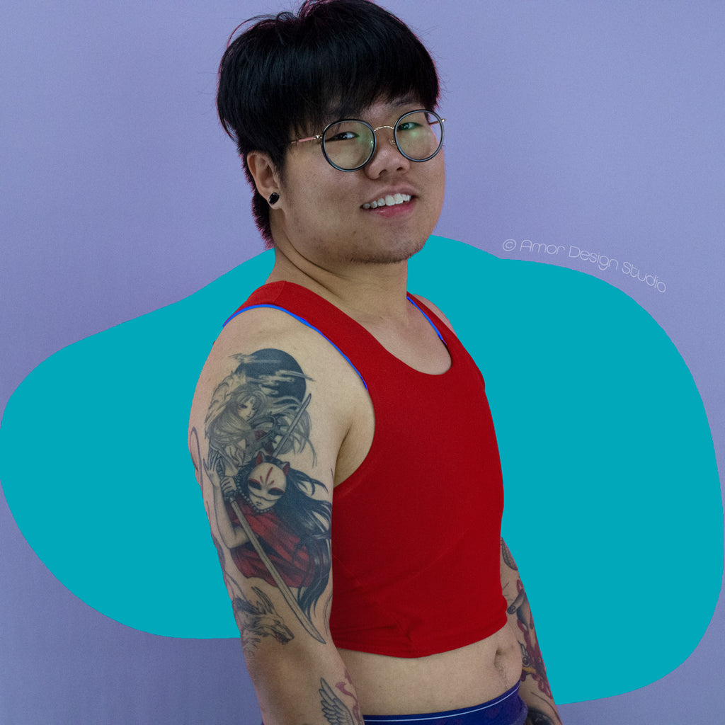Asian non-binary trans masc person wearing reversible chest binder worn on the red side. Colour is a fire engine red.. 