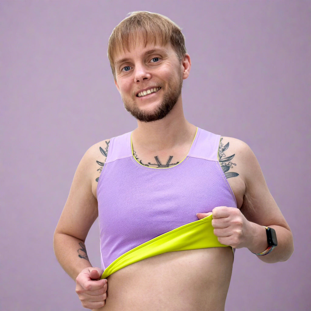 Non-binary person wearing lime and lilac coloured reversible chest binder