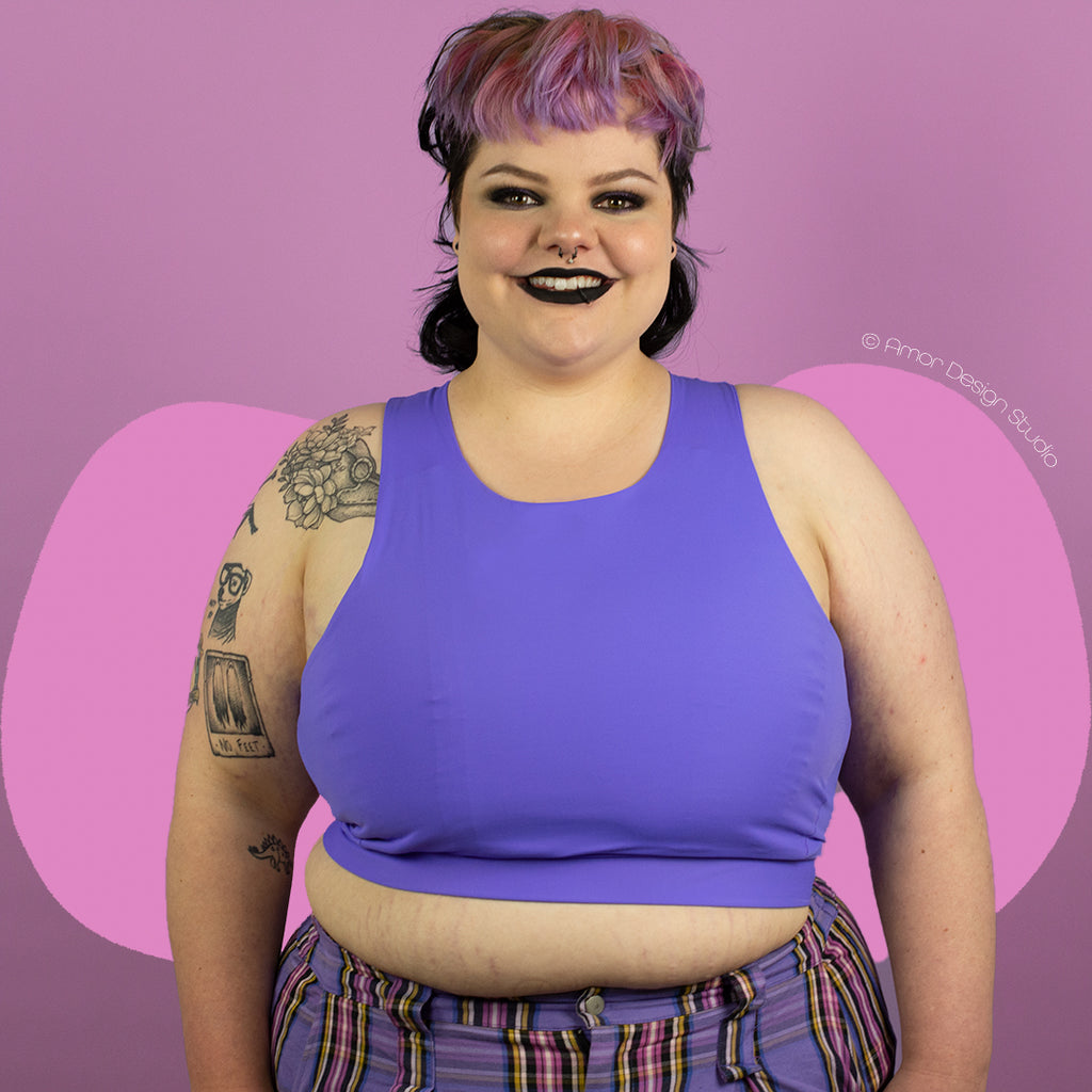 Plus size non-binary person wearing a purple, mid length, full chest binder - front