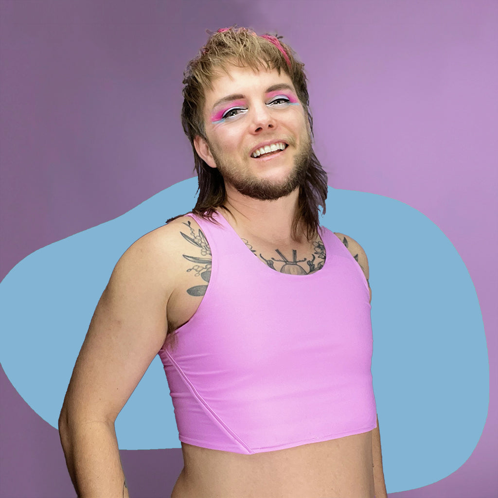 Nonbinary trans person wearing pastel pink chest binder, smiling.