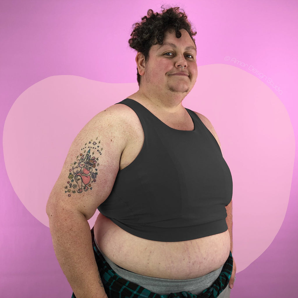 Plus size non-binary trans person wearing dark grey, mid length, full chest binder - side