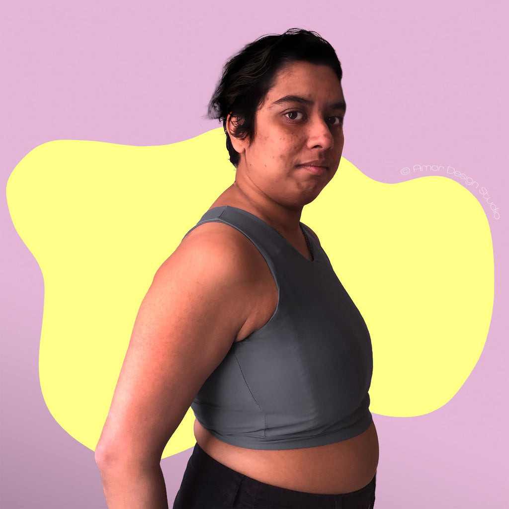 Non-binary person wearing a mid grey, mid length, full chest binder - side