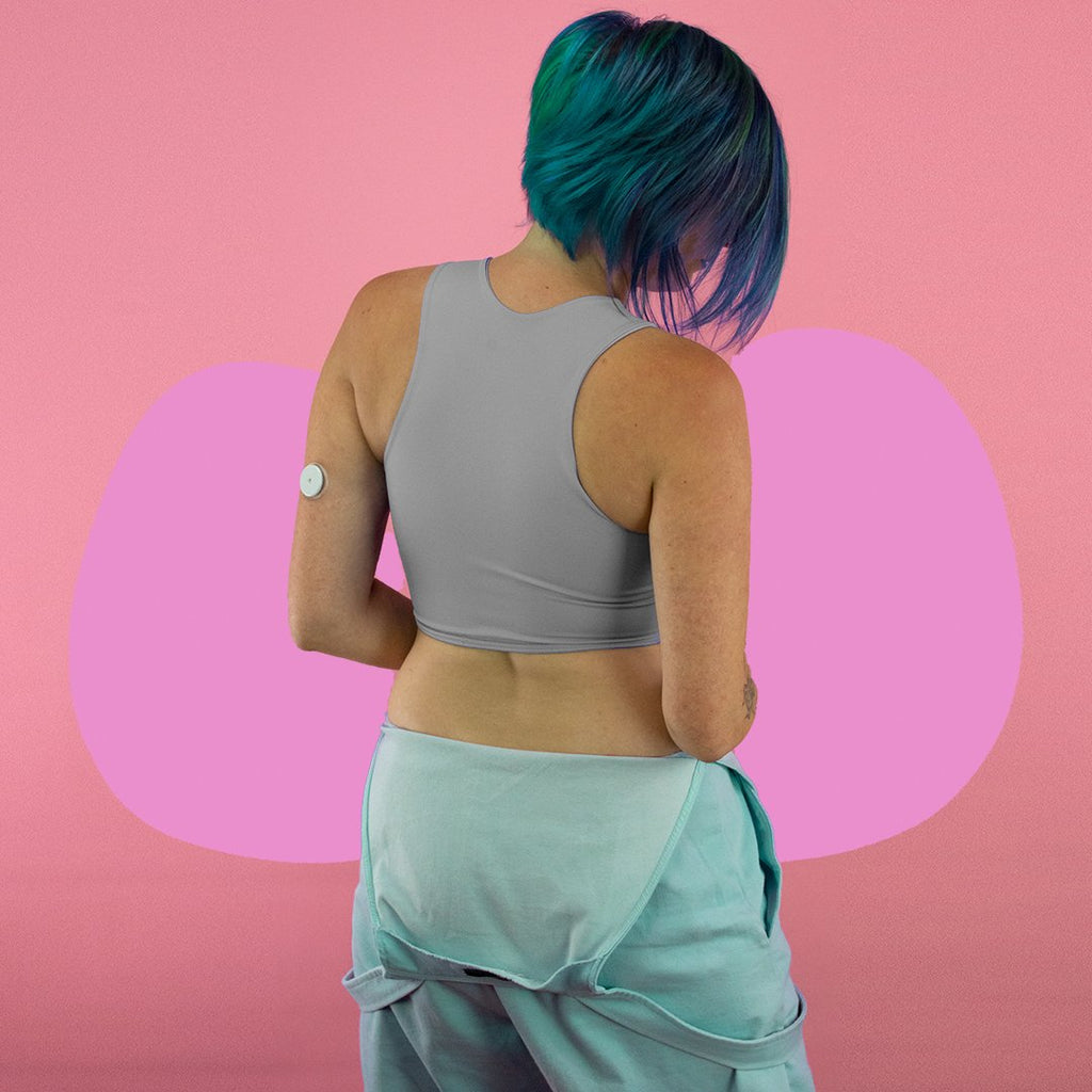 Non-binary person wearing a light grey, mid length, racerback chest binder - back
