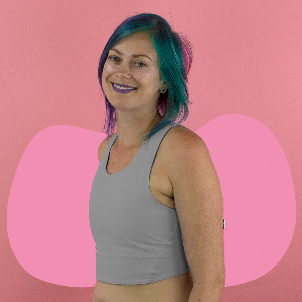 Non-binary person wearing a light grey, mid length, racerback Amor chest binder - side